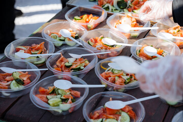 A person is carefully selecting a bowl filled with a fresh salad and using a plastic spoon to serve it, enjoying a nutritious meal that highlights vibrant greens and colorful vegetables
