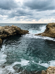 A serene body of sparkling blue water framed by rugged rocks and crashing waves creates a breathtaking scene on a cloudy day, showcasing the beauty of natures coastal landscape