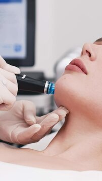 A cosmetologist doing a hydrofacial vacuum cleansing, rejuvenation, moisturizing procedure on a woman face in a modern beauty clinic. Concept of cosmetology, care and healthy skin. Vertical shot, ads