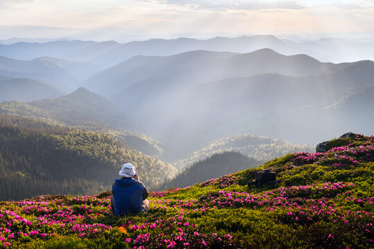 Landscape photographer capturing the view from a rhododendron-covered mountain edge, with a dreamy sunset sky and misty mountain ranges in the background