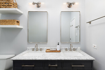 A bathroom detail with a dark grey cabinet, white marble countertop, and chrome light fixtures mounted above the two mirrors.