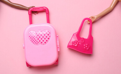 Hands of dolls holding travel luggage and bag on pink background