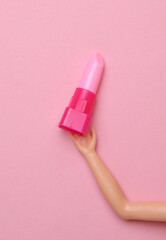 Lipstick in doll hand on a pink background