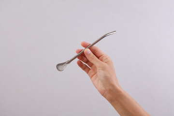 Female hand holding bombilla for mate on gray background.