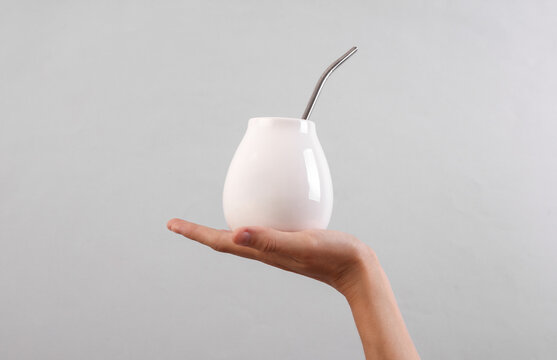 Female hand holding bombilla with white calabash for mate on gray background. Mockup for design
