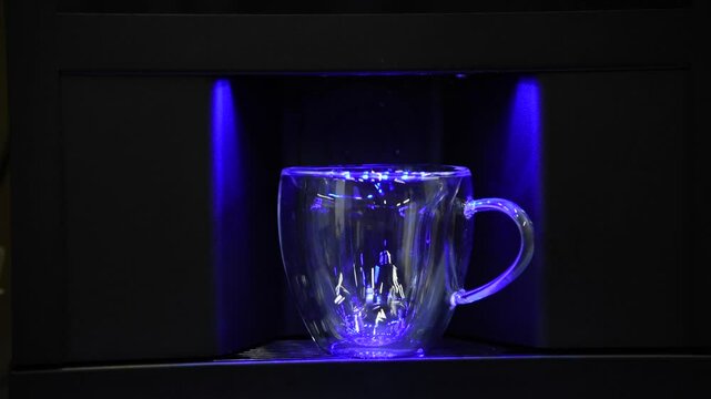 Close-up view of male person putting empty coffee cup (double wall glass thermo mug) in black automatic coffee machine or water cooler with blue LED light. Real time video.