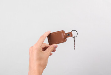Leather keychain with key in female hand on gray background