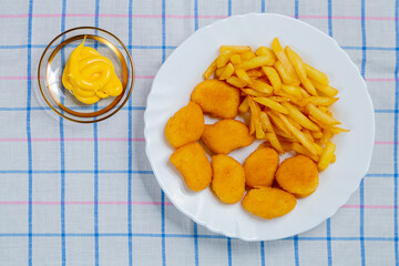 French fries and chicken crispy nuggets in a plate on a white checkered tablecloth