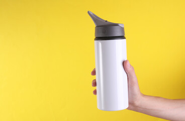 White metal water flask, thermos bottle in hand on yellow background. Mockup for design