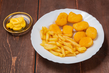French fries and golden chicken nuggets in a plate next to cheese sauce