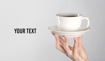 Female hands hold a white ceramic tea cup with a saucer on gray background. Copy space for your text and information