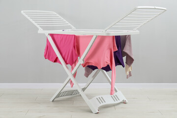 Drying rack with fresh clean laundry near grey wall