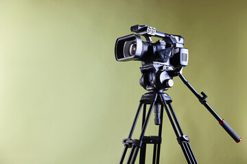 Modern video camera with tripod on light olive background, space for text