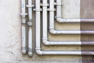 Old metal water and gas methane pipeline in front of an old plaster wall
