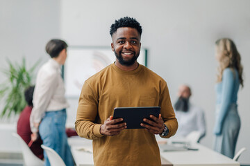 Smiling black businessman holding tablet in modern office with coworkers