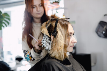 A professional hairstylist blow-drying and styling a client’s blonde hair in a modern salon setting.