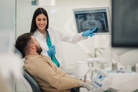 Female dentist showing teeth x ray to patient in modern clinic