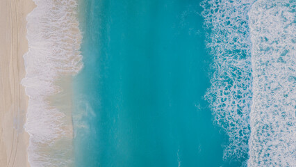 Aerial top-down view of the ocean waves gently rolling onto a pristine beach in Tulum, Mexico. The striking contrast of deep blue and foamy white waves creates a serene, minimalist seascape.