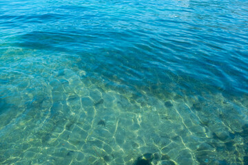 Clear turquoise water, sunlight reflecting, symbolizing natural beauty and serene aquatic scene, bottom through transparent water, blue background, natural resources planet