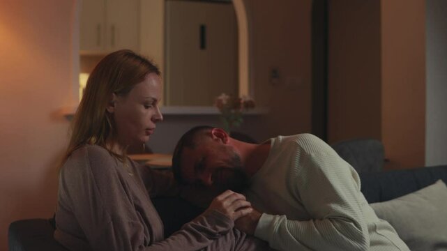 Pregnant woman tenderly supporting bearded partner, providing comfort while sitting closely on living room sofa during vulnerable emotional connection