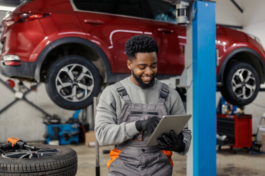 Portrait of smiling interracial auto mechanic scrolling on tablet at mechanic workshop.