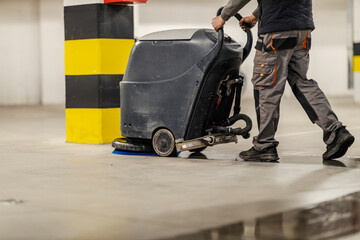 Cropped picture of worker washing garage floor with scrubber machine.