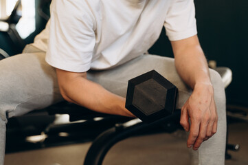 Obraz premium A trainer in a gym takes a black dumbbell with one hand and shows his students how to properly pump their biceps to avoid injury.
