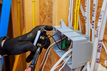Electrician contractor wearing gloves connects wires to switch light, installation in new home under construction.