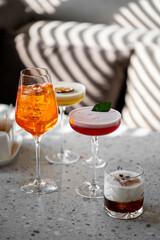 A set of four stylish cocktails on a terrazzo table: orange spritz, passion fruit, red with mint, and creamy coffee. Sunlight and shadows create an elegant, summery vibe.