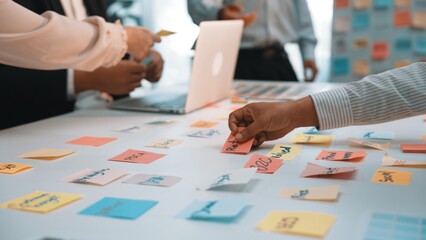 A dynamic office scene capturing a team engaged in a collaborative meeting, utilizing colorful sticky notes for brainstorming and idea generation around a laptop. SACTR