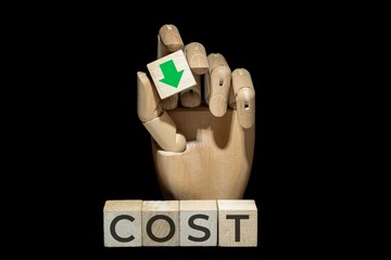 sztuczna ręka trzymająca kostkę z zieloną strzałką w dół nad napisem na kostkach: COST. Koncepcja poprawy rentowności poprzez obniżanie kosztów.