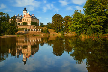 Fototapeta premium Picturesque Radun castle with tower reflected in calm lake waters during golden sunset, Czech Republic.