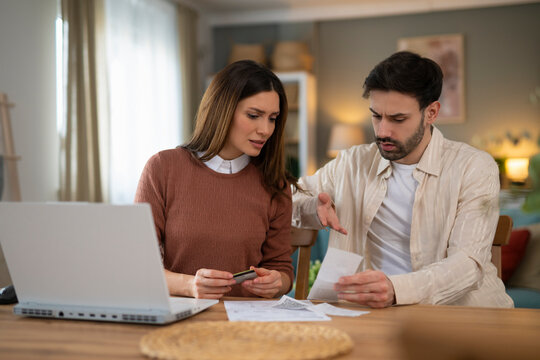 Young stressed Caucasian couple facing financials troubles, sitting at kitchen table with papers