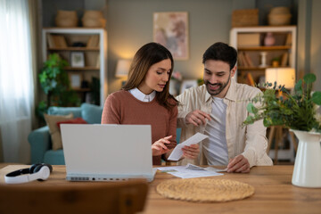 A guy and a girl look at the bills together and pay. Using a laptop to pay online