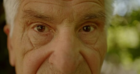 Close-up of an elderly man with white hair and wrinkles, looking directly into the camera.