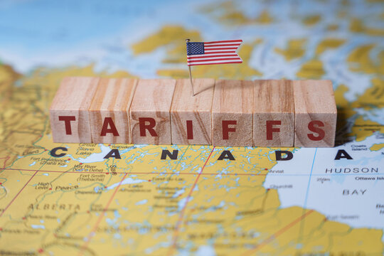 Wooden blocks spelling TARIFFS with a small U.S. flag on top, placed on a map highlighting Canada, symbolizing trade policies and economic relations