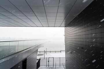Modern exterior of the building. A portable bridge for walks against the background of a river in a snowfall in the arch of the building.