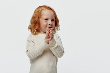 Innocent little girl with red hair standing in front of a white background clapping her hands