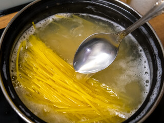 Cooking Spaghetti in Simmering Water, Using a Spoon to Stir and Enhance Flavorful Sauce