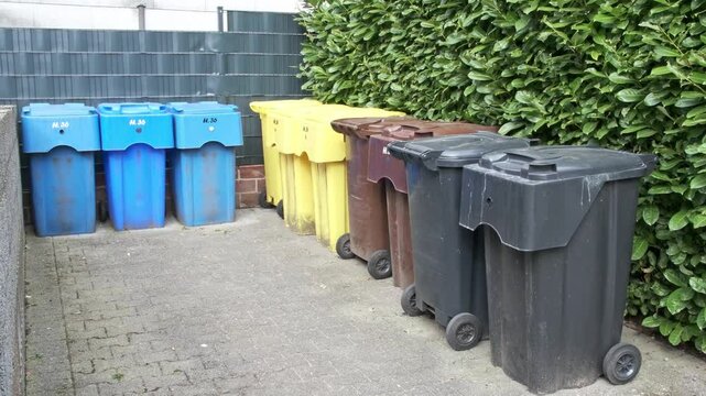 Trash cans on wheels in different colors - blue, yellow, brown, black, intended for waste sorting, stand on the street in Germany. The concept of proper waste sorting and ecology.