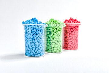 Blue, green and red masterbatch granules in measuring cup isolated on white background, color...