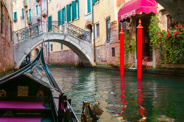 The romantic canals of Venice, Italy, featuring a traditional gondola ride under a historic stone bridge, colorful buildings with ivy-covered facades, and a charming waterside restaurant with red moor