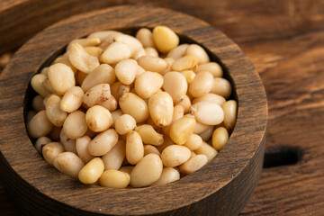 Pine nuts in wooden bowl on wooden background closeup.