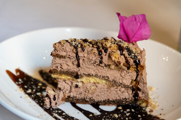 Portion of truffle chocolate tart decorated with a bouganvillea flower on white plate 