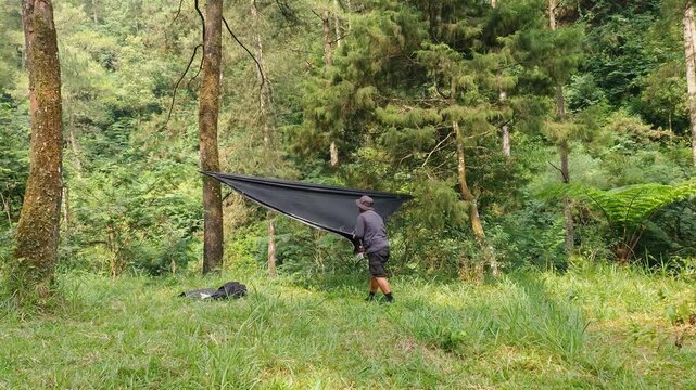 The process of setting up a shelter tent using a flysheet in the forest by a male adventurer. A traveler is setting up a flysheet for a bushcraft adventure in a pine forest area.