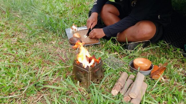 A male adventurer is cooking sauce to make a burger under a flysheet in the dense forest. The concept of bushcraft camping in a dense pine forest for adventure and cooking with simple equipment