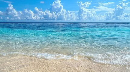 Waves softly roll onto a pristine beach with fine sand. The bright blue ocean stretches into the horizon, dotted with fluffy white clouds. Perfect weather invites relaxation and enjoyment
