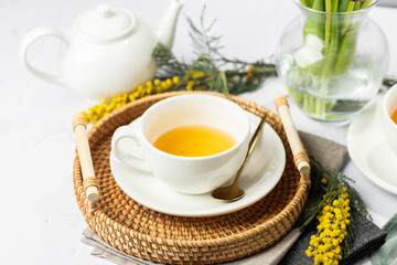 Green tea in a white porcelain cups and teapot, tulips in a glass vase, mimosa flowers, light background. Tea party.