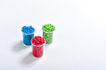 Blue, green and red masterbatch granules in measuring cup isolated on white background, color...