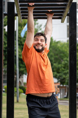 Hombre sonriente entrenando haciendo balanceos en barras. Entrenamiento al aire libre. Fotografía...